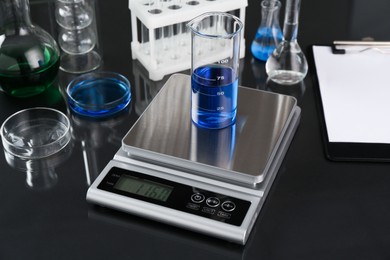 Photo of Scale with beaker of sample and other laboratory glassware on black mirror table, closeup