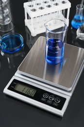 Photo of Scale with beaker of sample and other laboratory glassware on black mirror table, closeup