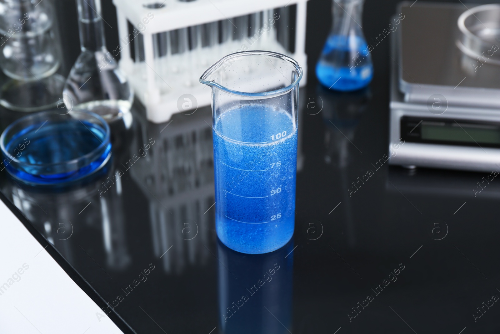 Beaker with blue liquid, other laboratory glassware and scale on black mirror table, closeup Photo of Beaker with blue liquid, other laboratory glassware and scale on black mirror table, closeup