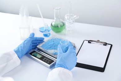 Photo of Scientist weighing sample on scales at white table, closeup