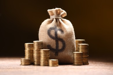 Photo of Bag with dollar sign and stacked coins on table against dark background
