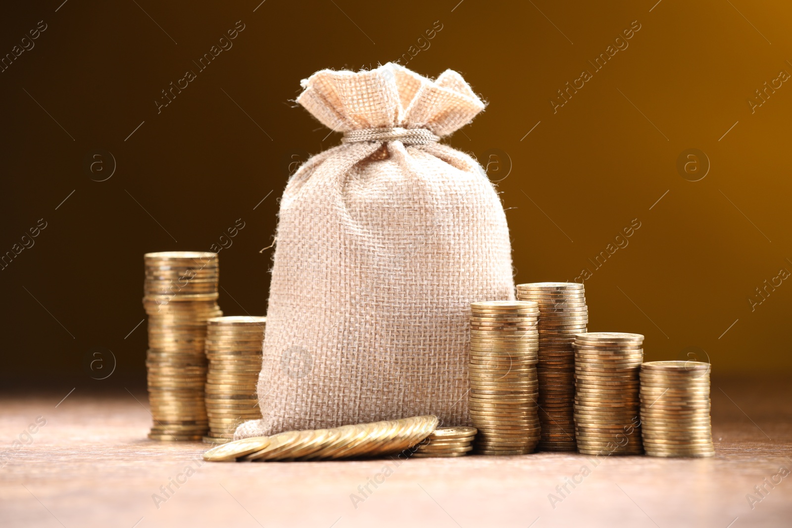 Bag and stacked coins on table against color gradient background Photo of Bag and stacked coins on table against color gradient background