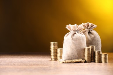 Photo of Bags and stacked coins on wooden table against dark yellow gradient background, space for text