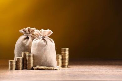 Photo of Bags and stacked coins on wooden table against dark yellow gradient background, space for text