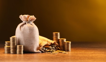 Photo of Bags and stacked coins on wooden table against dark yellow gradient background, space for text