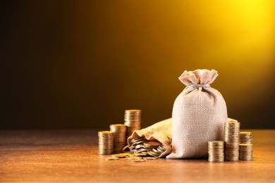 Photo of Bags and stacked coins on wooden table against dark yellow gradient background, space for text