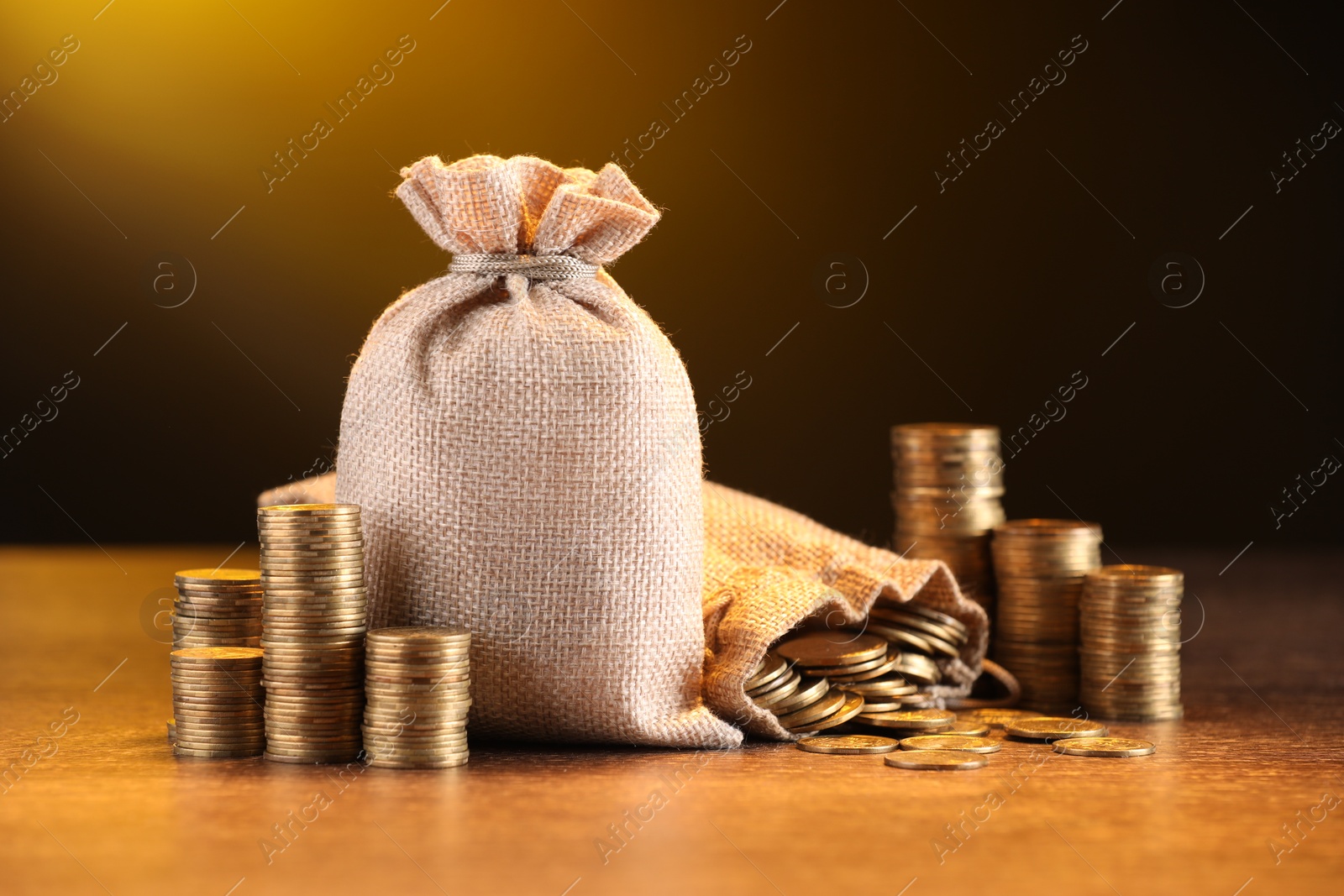 Bags and stacked coins on wooden table against dark yellow gradient background Photo of Bags and stacked coins on wooden table against dark yellow gradient background