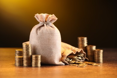 Photo of Bags and stacked coins on wooden table against dark yellow gradient background