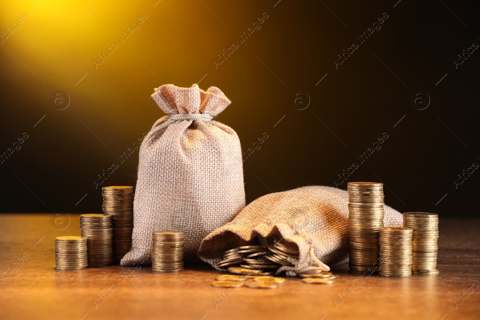 Bags and stacked coins on wooden table against dark yellow gradient background Photo of Bags and stacked coins on wooden table against dark yellow gradient background