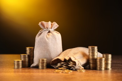 Photo of Bags and stacked coins on wooden table against dark yellow gradient background