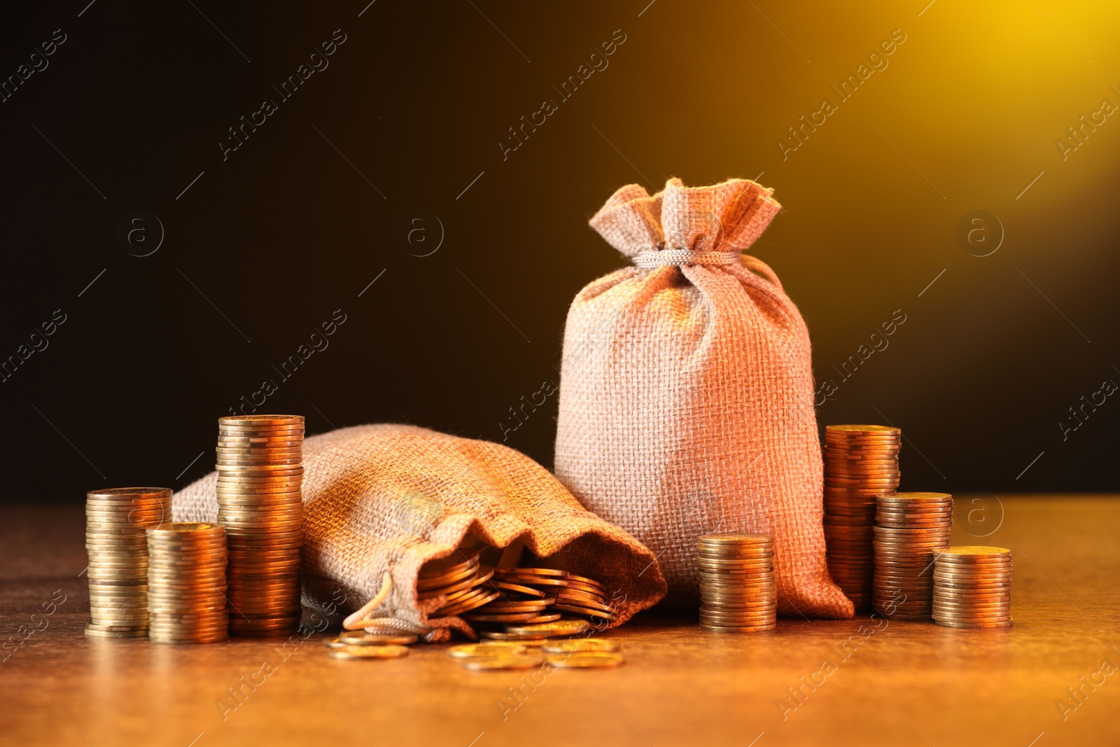 Bags and stacked coins on wooden table against dark yellow gradient background Photo of Bags and stacked coins on wooden table against dark yellow gradient background