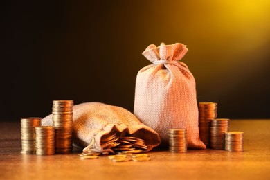 Photo of Bags and stacked coins on wooden table against dark yellow gradient background
