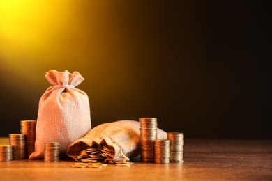 Photo of Bags and stacked coins on wooden table against dark yellow gradient background, space for text