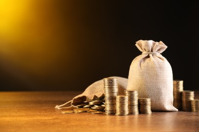 Photo of Bags and stacked coins on wooden table against dark yellow gradient background, space for text