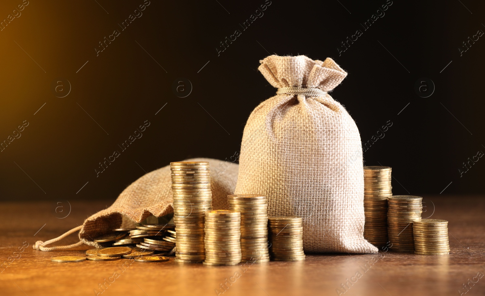 Bags and stacked coins on wooden table against dark yellow gradient background Photo of Bags and stacked coins on wooden table against dark yellow gradient background