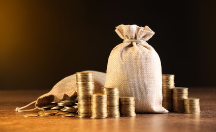 Photo of Bags and stacked coins on wooden table against dark yellow gradient background