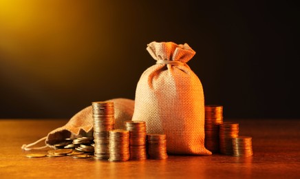 Photo of Bags and stacked coins on wooden table against dark yellow gradient background