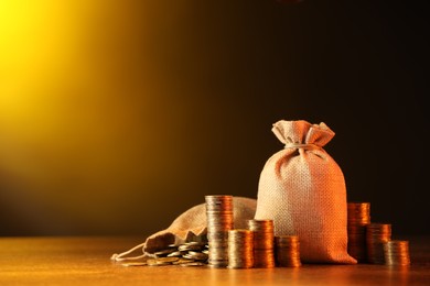 Photo of Bags and stacked coins on wooden table against dark yellow gradient background, space for text