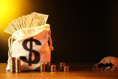 Photo of Bags with dollar banknotes and stacked coins on wooden table against dark yellow gradient background, space for text
