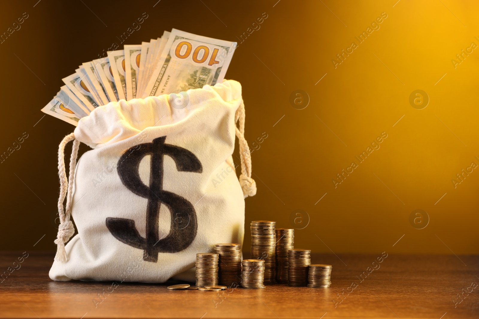 Bag with dollar banknotes and stacked coins on wooden table against yellow gradient background, space for text Photo of Bag with dollar banknotes and stacked coins on wooden table against yellow gradient background, space for text