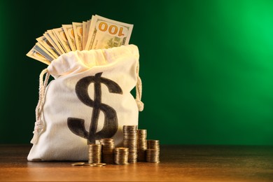 Photo of Bag with dollar banknotes and stacked coins on wooden table against green gradient background, space for text