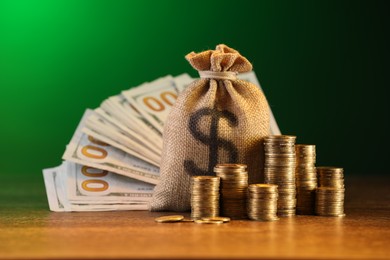 Photo of Bag, dollar banknotes and stacked coins on wooden table against green gradient background