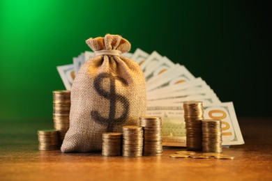 Photo of Bag, dollar banknotes and stacked coins on wooden table against green gradient background