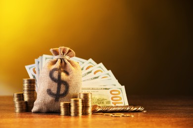 Photo of Bag, dollar banknotes and stacked coins on wooden table against yellow gradient background, space for text