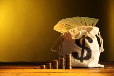 Photo of Bag with dollar banknotes and stacked coins on wooden table against yellow gradient background, space for text