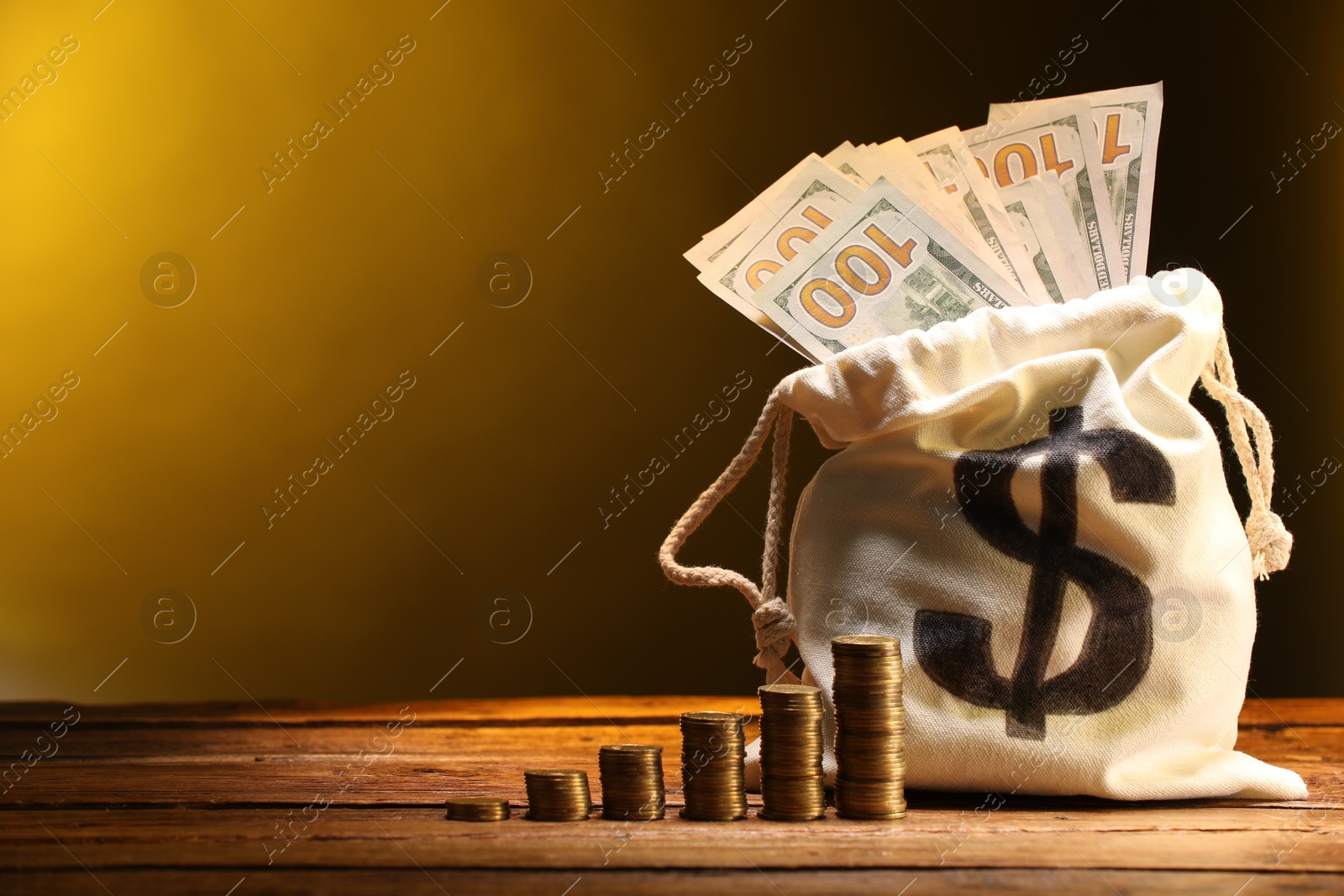 Bag with dollar banknotes and stacked coins on wooden table against yellow gradient background, space for text Photo of Bag with dollar banknotes and stacked coins on wooden table against yellow gradient background, space for text