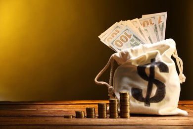 Photo of Bag with dollar banknotes and stacked coins on wooden table against yellow gradient background, space for text
