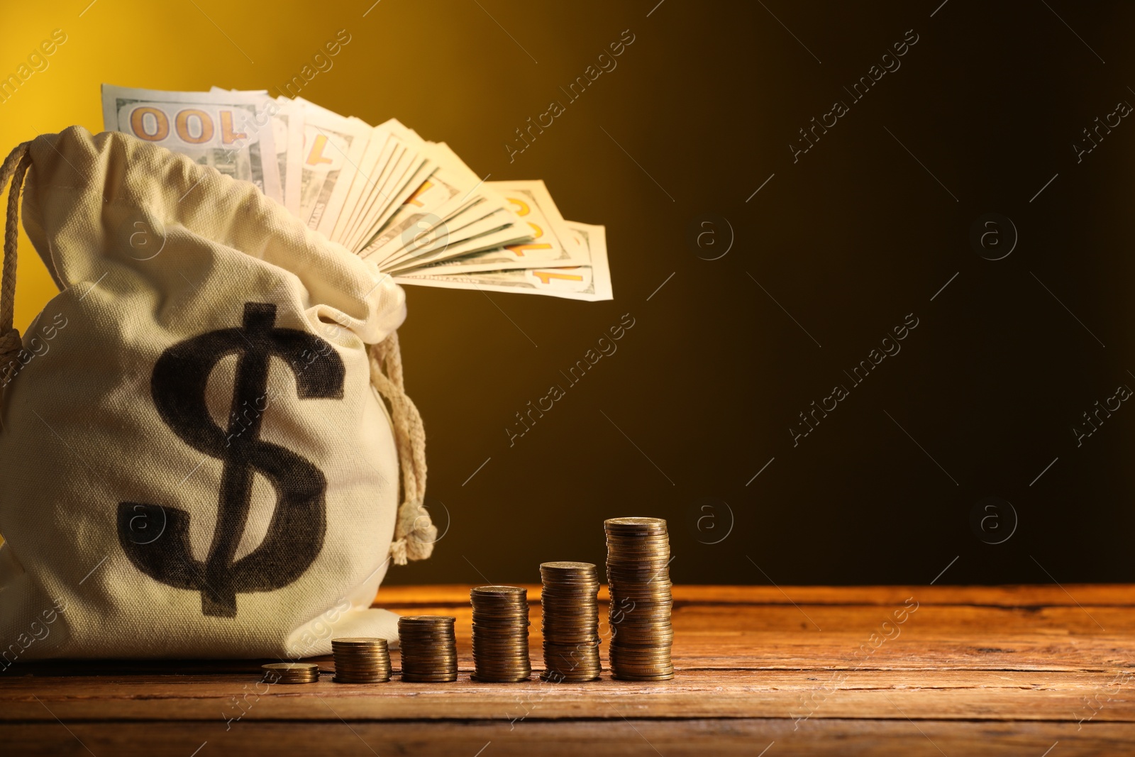 Bag with dollar banknotes and stacked coins on wooden table against yellow gradient background, space for text Photo of Bag with dollar banknotes and stacked coins on wooden table against yellow gradient background, space for text