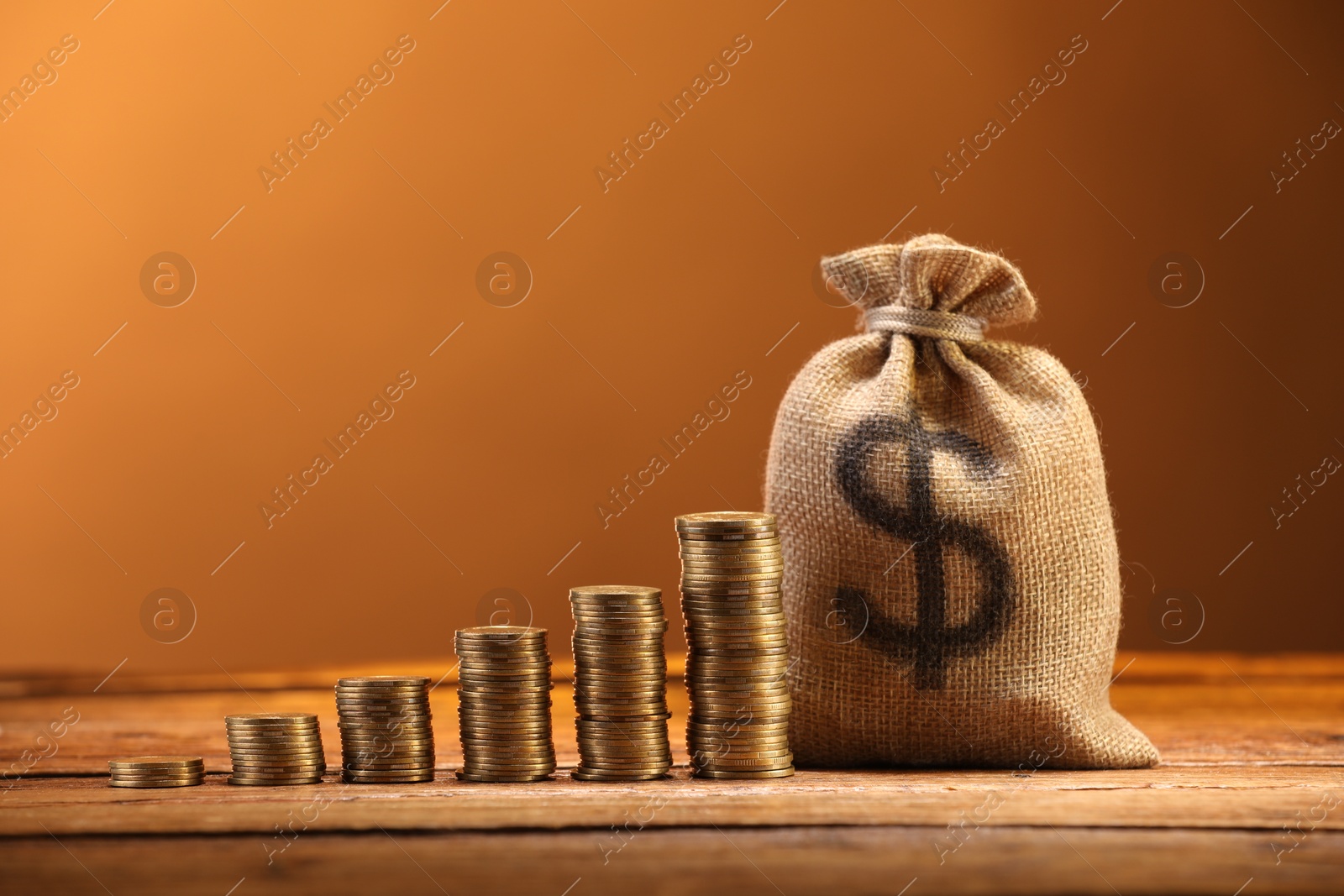 Bag with dollar sign and stacked coins on wooden table against brown background Photo of Bag with dollar sign and stacked coins on wooden table against brown background