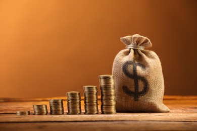 Photo of Bag with dollar sign and stacked coins on wooden table against brown background