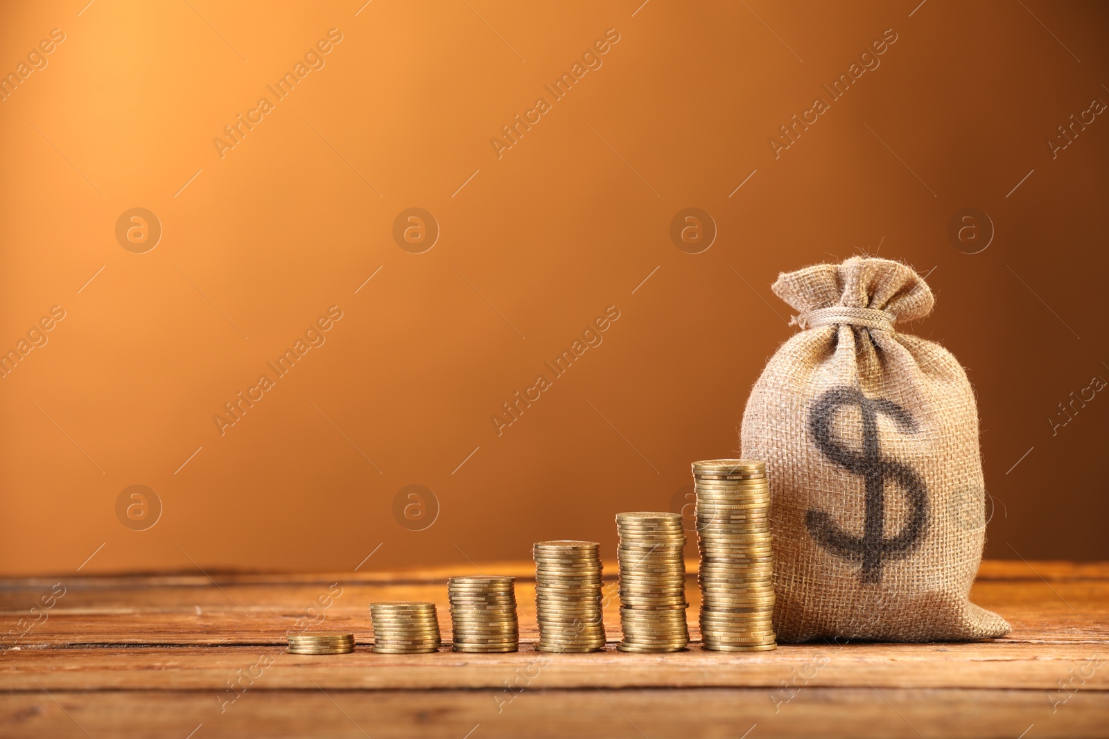 Bag with dollar sign and stacked coins on wooden table against brown background, space for text Photo of Bag with dollar sign and stacked coins on wooden table against brown background, space for text