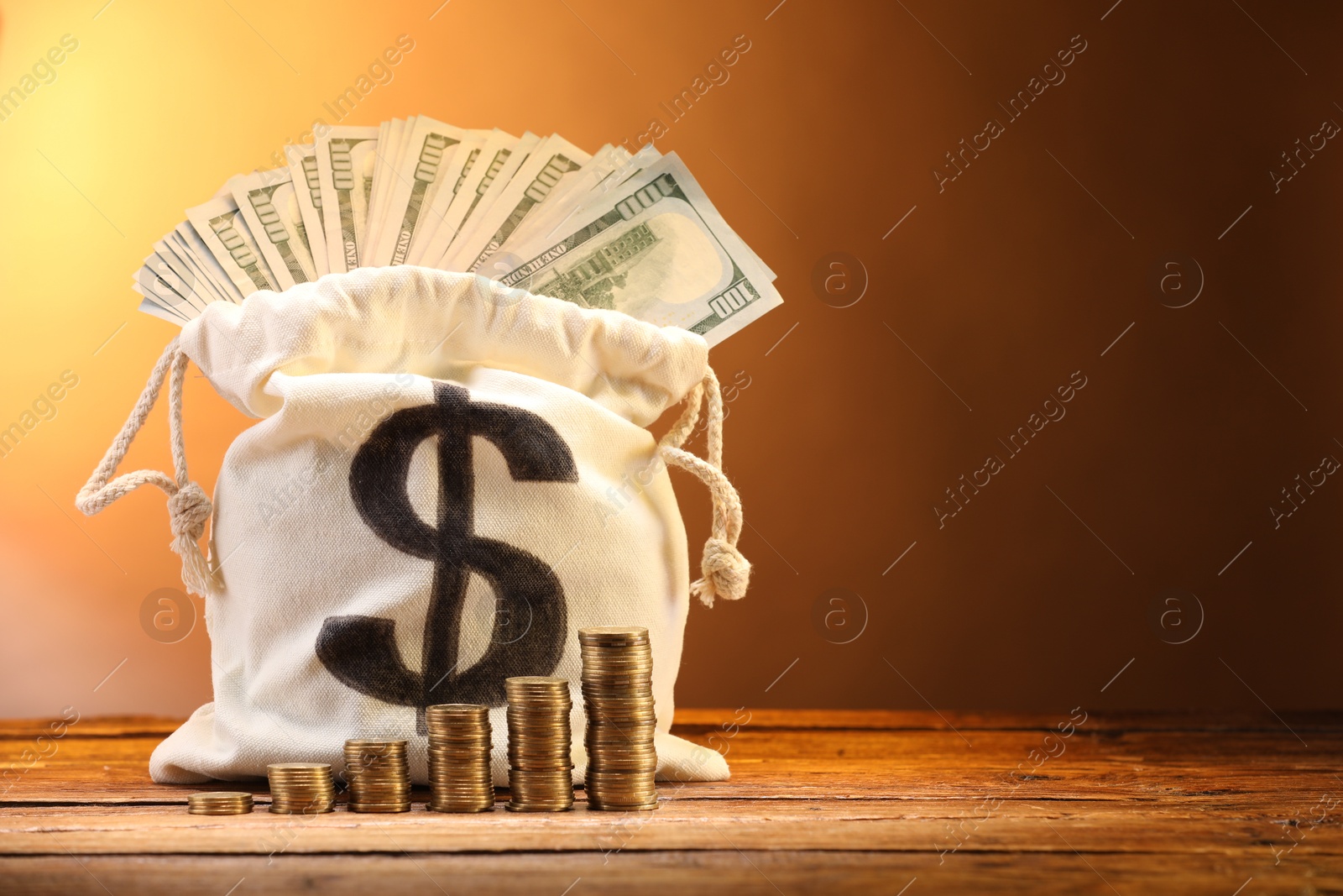 Bag with dollar banknotes and stacked coins on wooden table against brown gradient background, space for text Photo of Bag with dollar banknotes and stacked coins on wooden table against brown gradient background, space for text