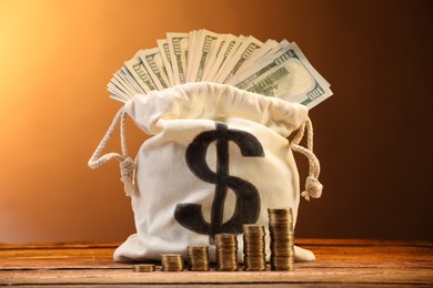 Photo of Bag with dollar banknotes and stacked coins on wooden table against brown gradient background