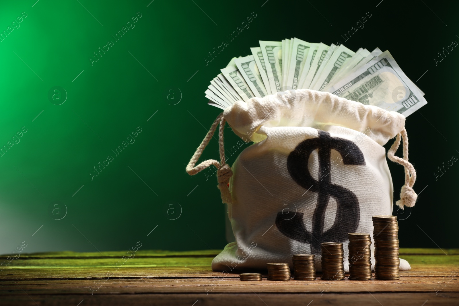 Bag with dollar banknotes and stacked coins on wooden table against green gradient background, space for text Photo of Bag with dollar banknotes and stacked coins on wooden table against green gradient background, space for text