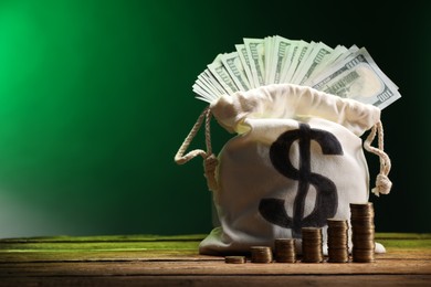 Photo of Bag with dollar banknotes and stacked coins on wooden table against green gradient background, space for text