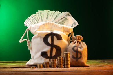 Photo of Bags with dollar banknotes and stacked coins on wooden table against green gradient background