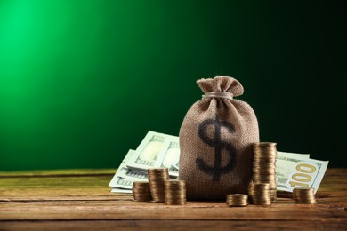 Photo of Bag, dollar banknotes and stacked coins on wooden table against green gradient background, space for text