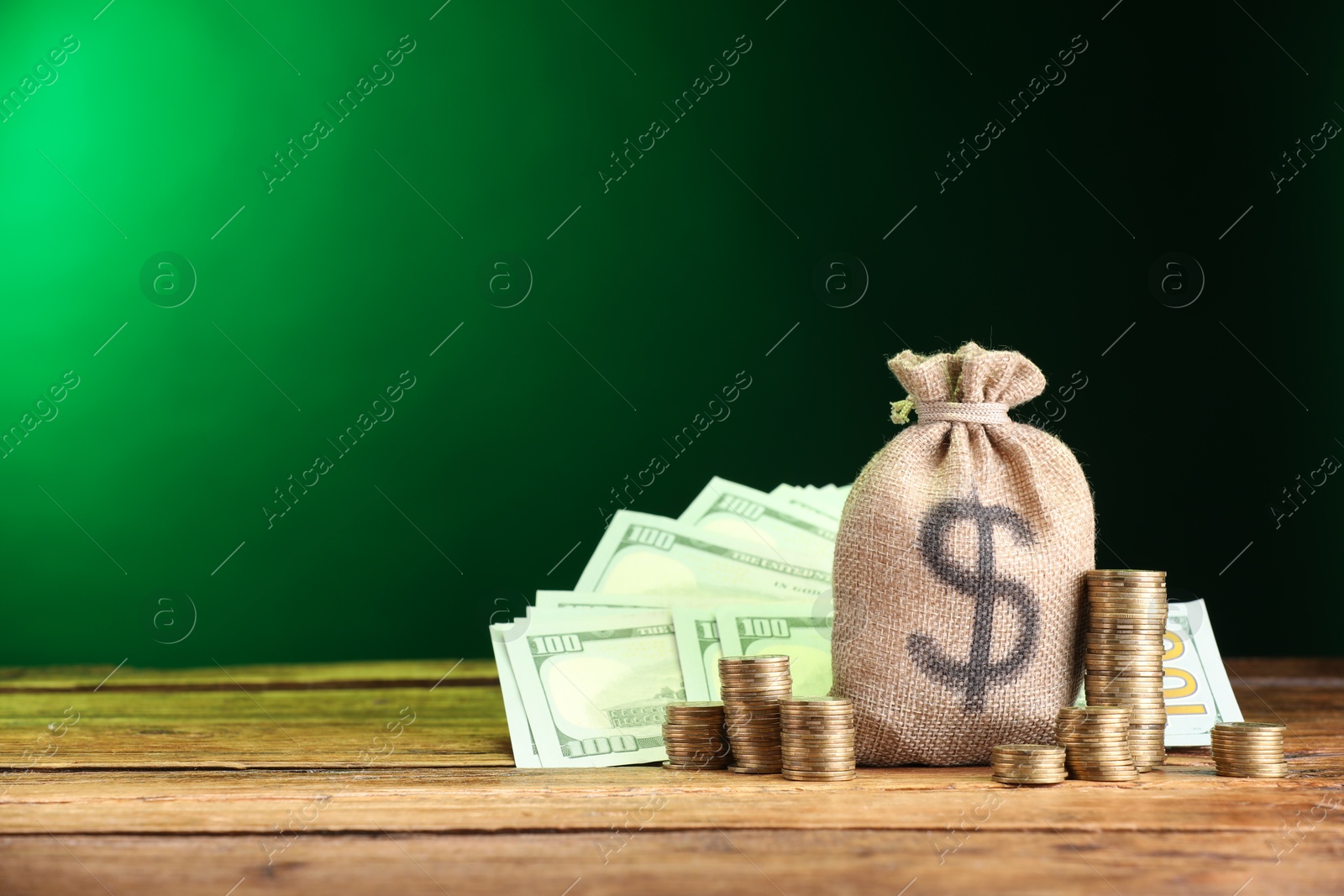 Bag, dollar banknotes and stacked coins on wooden table against green gradient background, space for text Photo of Bag, dollar banknotes and stacked coins on wooden table against green gradient background, space for text