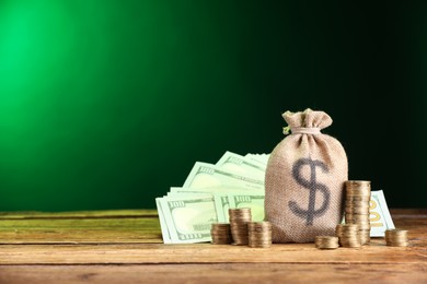 Photo of Bag, dollar banknotes and stacked coins on wooden table against green gradient background, space for text