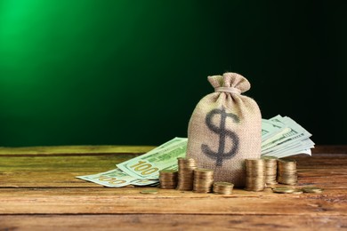 Photo of Bag, dollar banknotes and stacked coins on wooden table against green gradient background, space for text