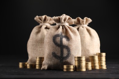 Photo of Bags with dollar sign and stacked coins on black table against dark background