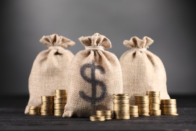 Photo of Bags with dollar sign and stacked coins on black table against gray background