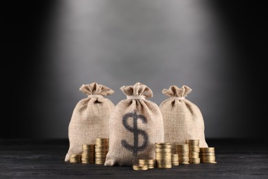 Photo of Bags with dollar sign and stacked coins on black wooden table against gray gradient background