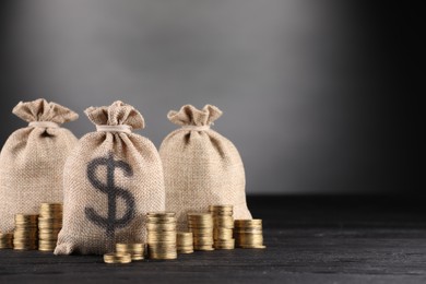 Photo of Bags with dollar sign and stacked coins on black wooden table against gray gradient background, space for text