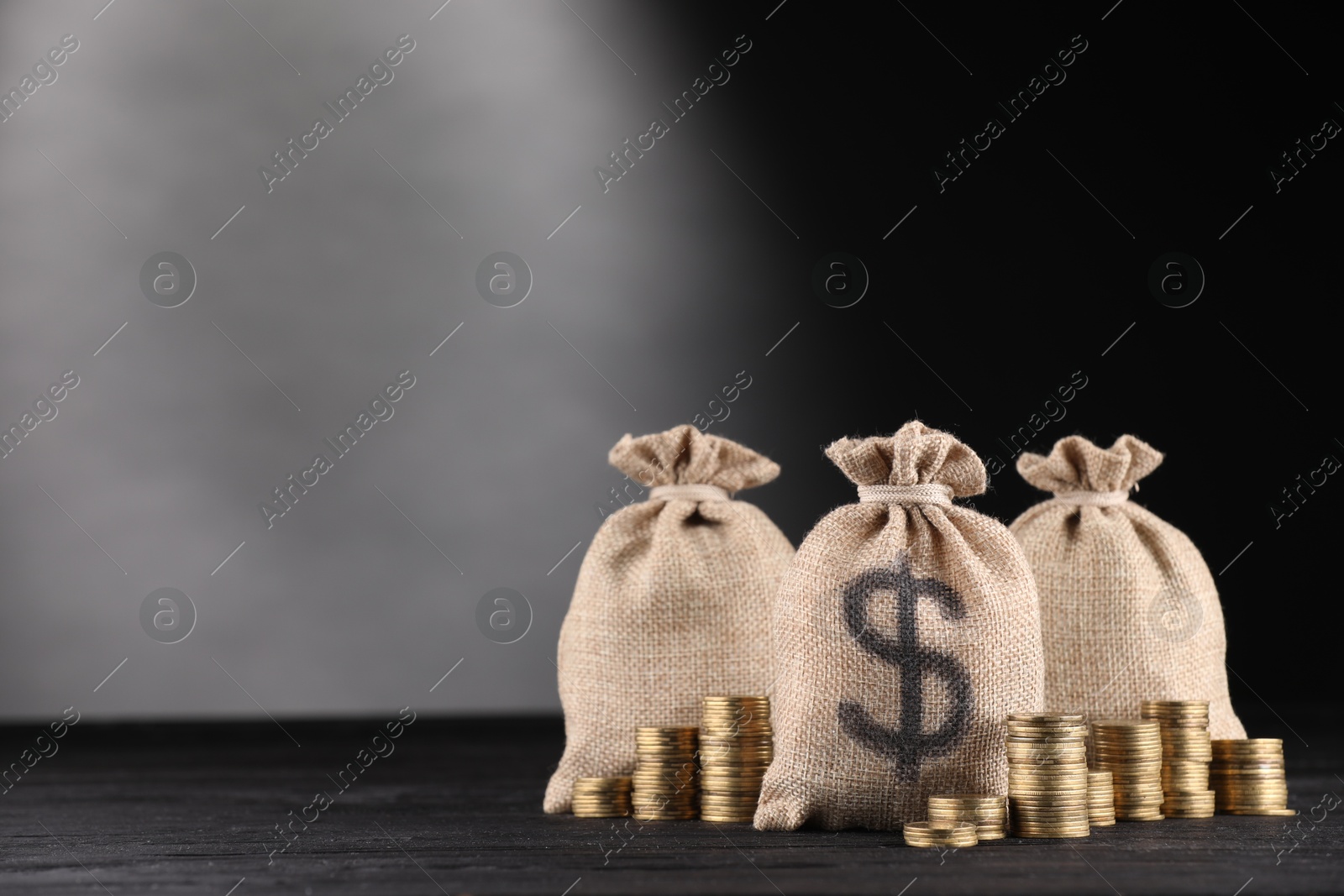Bags with dollar sign and stacked coins on black wooden table against gray gradient background, space for text Photo of Bags with dollar sign and stacked coins on black wooden table against gray gradient background, space for text