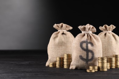 Photo of Bags with dollar sign and stacked coins on black wooden table against gray gradient background, space for text